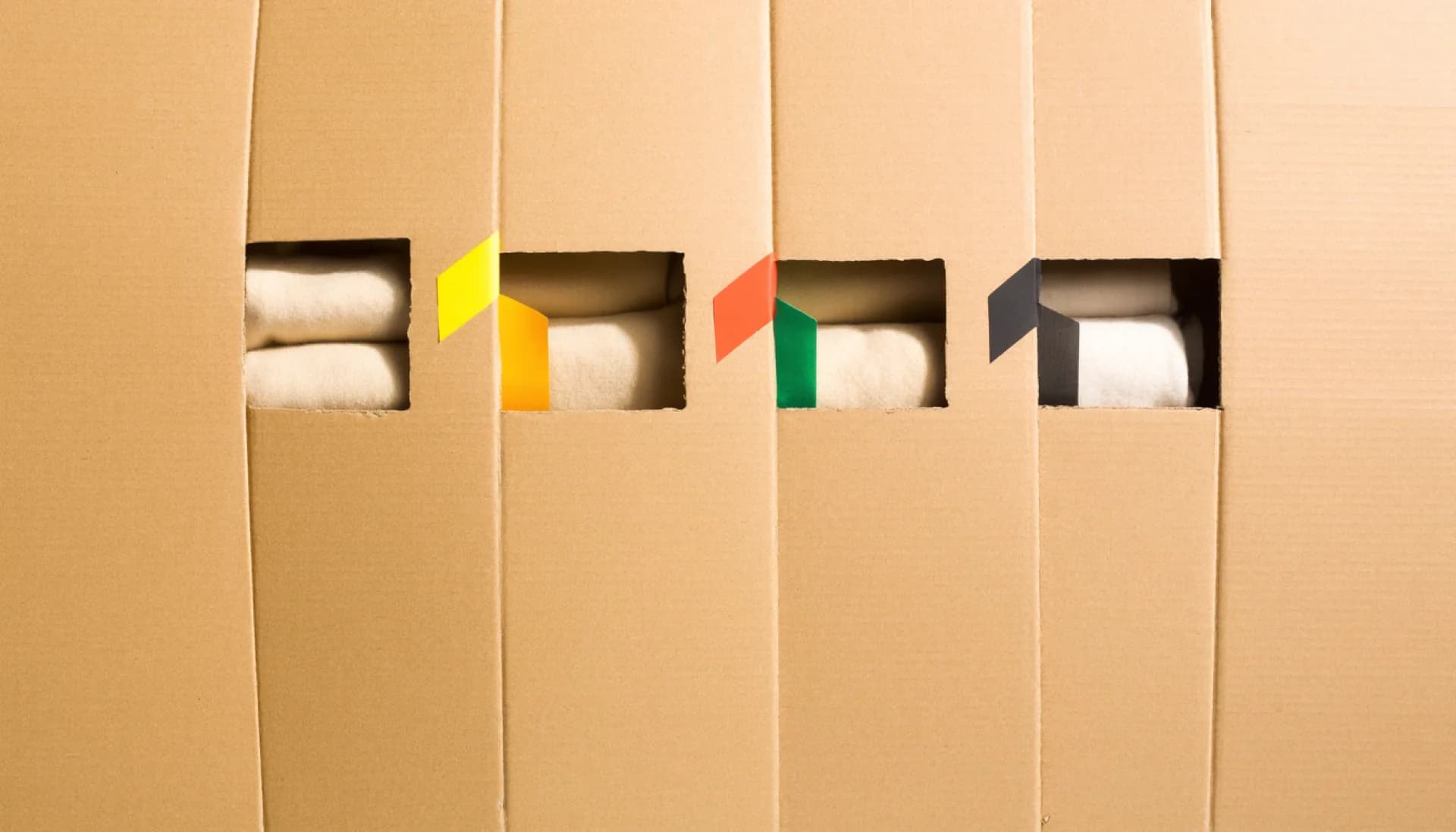 Folded basics laid out in four groups on raw cardboard, divided by strips of yellow, orange, green and black tape.