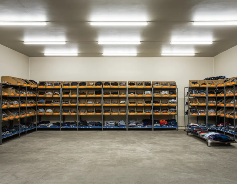 Interior of a small clothing shop with folded clothes stacked in open cardboard crates on metal shelving.